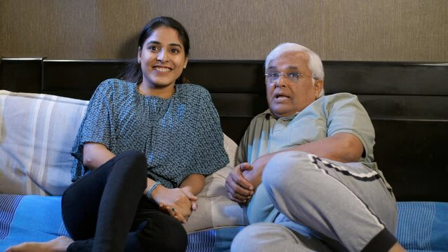 An aged gentleman and his young daughter are watching television together - father daughter bonding. A beautiful girl in her early twenties is watching Tv with her grandfather - generation gap  com...