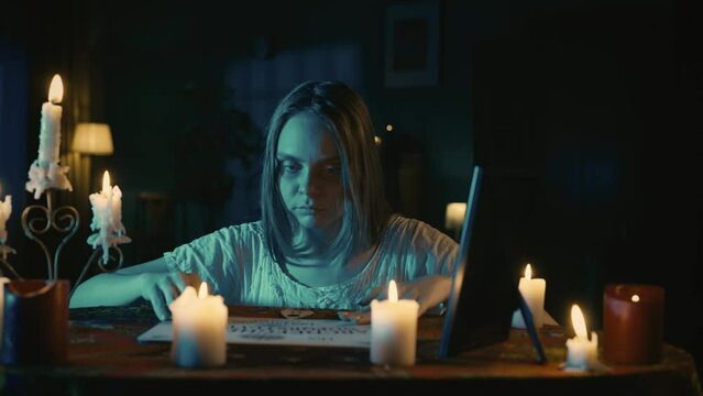 Video of a young woman sitting at the table, having ouija board session. Paranormal activity begins to show, planchette moves actively, candles are blown.