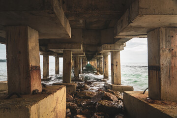 A bottom view of a rocky coast boarding an old pier during a dramatic sunset. - 643565357