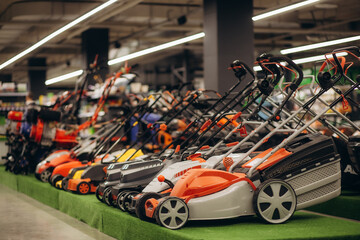 Showcase of the new powerful red gasoline lawn mower in the store (shop). Indoor shoot with nobody. - obrazy, fototapety, plakaty