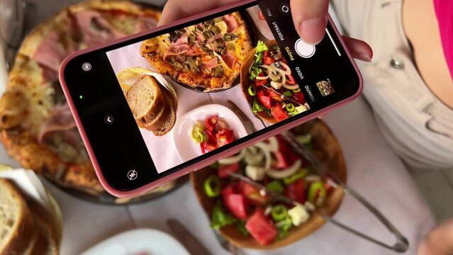 taking photos of food on social. networks with iPhone pizza caesar salad bread on the table restaurant teenagers New generation of gadget phones video upright girl useful food