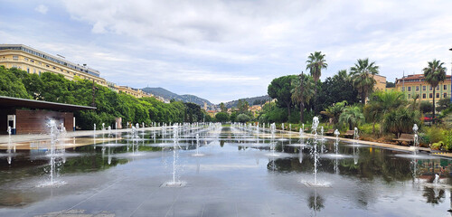 City fountain in the square, park in the city of Nice main square, Place Massena, during the day. Panoramic view of the mountainous part of the city, view on zoom. Cote d'Azur, France