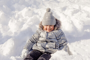 Little girl playing with snow in the winter park. Winter activities for children. Cute kid has fun ourdoor in winter park