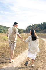 A man and a woman walk into a field holding hands.