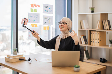 Muslim female with mobile on stick filming video in office