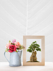 Bonzai tree in wooden frame with paper rose flower vase on white background with leaf texture, decoration item