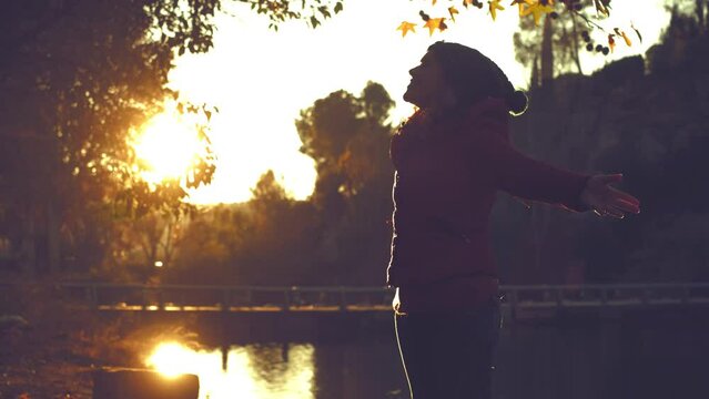 People enjoying having fun in autumn season at the park. One happy overjoyed woman throwing leaves in the air and outstretching ars with big smile expression on face. Natural lifestyle lady enjoy life