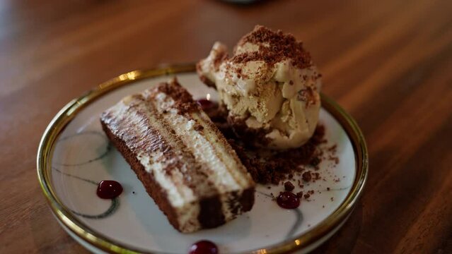 an ice cream dessert is accompanied by a slice of tiramisu cake. The creamy ice cream and rich cake unite, promising a symphony of flavors that captivates the palate. High quality 4k footage
