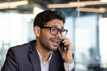 Dissatisfied and upset man talking on phone close up, businessman young in business clothes at workplace inside office.