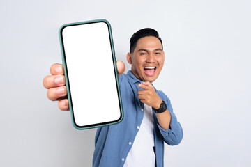 Excited young Asian man in casual shirt showing smartphone with blank screen isolated on white...