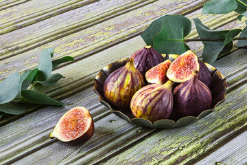 Fresh ripe figs in vintage plate, sprigs of green eucalyptus as decoration. Close up view