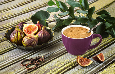 Fresh ripe figs on vintage plate, purple cup of coffee, sprig of eucalyptus, vintage scissors as decor on wooden background.