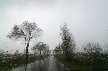 Fototapeta na wymiar Vista otoñal de la carretera con lluvia desde el interior de un vehículo con agua en el parabrisas.