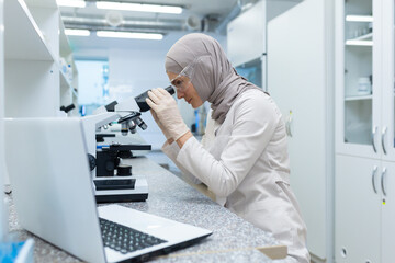 Young Muslim woman in hijab. a scientist, a pharmacist, a doctor works in a laboratory. Sits at the...