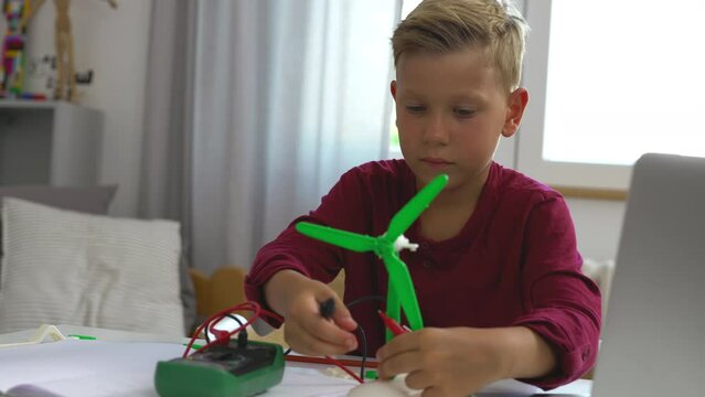 A boy is connecting cable between generator and a windmill model for a school science project.