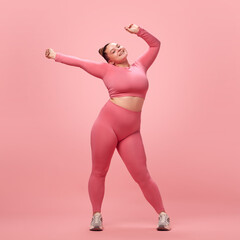Full length happy young attractive plus size active woman in pink top and leggins warm up, training...