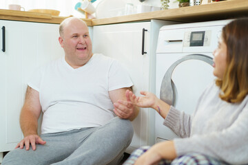 Obraz premium Lovely diverse ethnicity husband and wife putting a used clothes into the automatic washing machine. Lovely happy couple working or doing their housework - chores together.