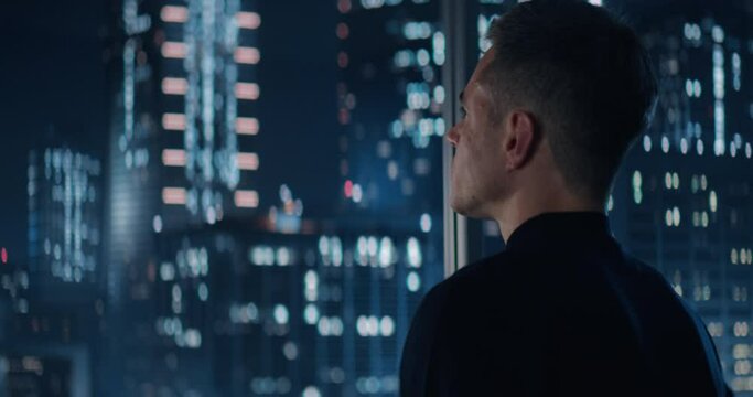 Close Up Portrait of Caucasian Businessman in a Suit Standing Next to Window in Big City Office with Skyscrapers Late At Night. Male General Manager Looking Out Of Window Thoughtfully.