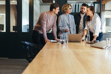 Design team discussing a project in a meeting, they're standing together around a laptop in a...