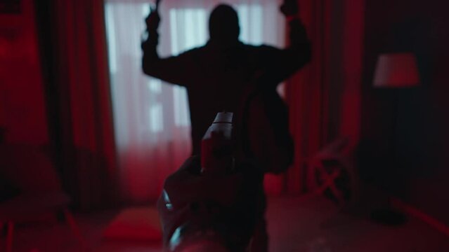The arrest of a robber at the crime scene, in a dark apartment lit with blue red light. First person view of a hand with a pistol aimed at a criminal close up.