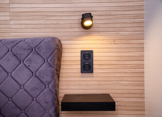 Shelf and socket for the phone near the bed in the bedroom. Swivel lamps at the head of the bed, interior.