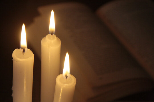 The burning candles close up with the blurred book. A warm atmosphere in the dark room.