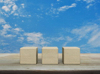 Three wood block cubes on wooden table over blue sky with white clouds