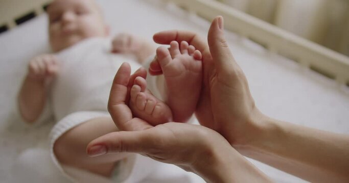 Selective focus on infant baby tiny feet in mother hands. Mom female touching adorable newborn legs and massaging toes. Parenthood concept