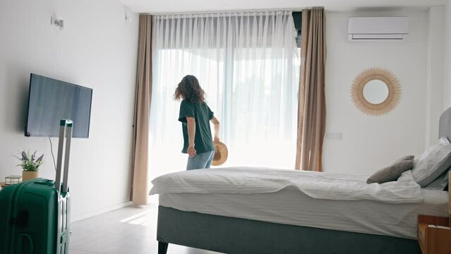 Satisfied woman traveler jumping onto the bed in hotel bedroom after check-in and rejoicing travelstart. Enjoy holiday and vacation. Happy moment
