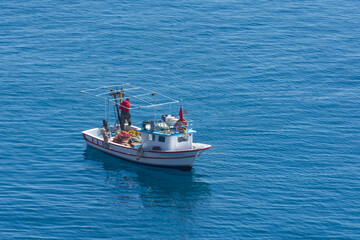 Small fishing boat with nets follows the sea surface of the Mediterranean Sea view from above aerial away distance.