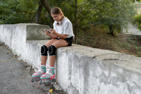 Young skater playing mobile game on a smart phone in a skatepark. Roller blader female sitting on a ledge with a gamepad attached to a mobile phone