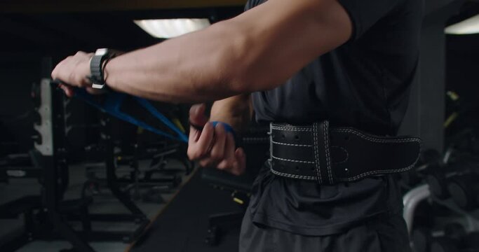 Closeup on bodybuilder male hand wrapping lifting wrist straps for weight training. Cropped view on athletic man preparing for strength workout at gym 