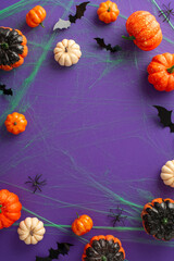 Hauntingly Alluring Halloween: Vertical top view capture of themed embellishments, crawly critters such spiders, pumpkins, eerie green spiderweb, bats on purple setting, empty frame for text insert