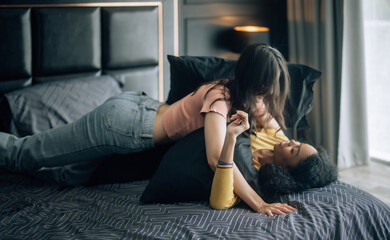 Lesbian partners share joy, play on bed, embrace, exchange tender kiss, radiating genuine happiness