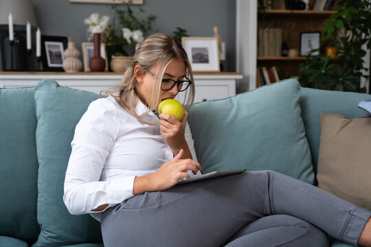 Young businesswoman after work sitting on sofa at home reading statistics on tablet, preparing and informing for the next working day.