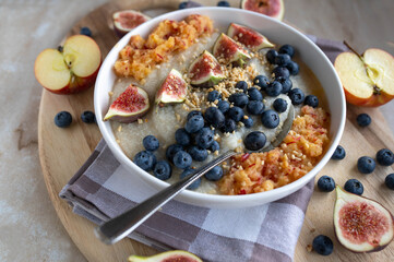 Millet porridge with fresh fruits such as grated apples, figs and blueberries in a bowl with spoon