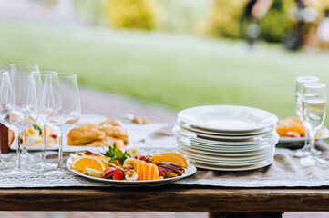 A round plate with a variety of fruits, champagne glasses, empty dishes stand on a wooden table at a banquet. Photo of food, dessert, buffet at the holiday.