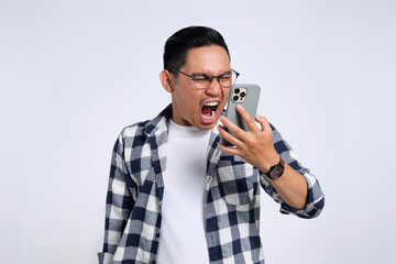 Angry young Asian man in casual shirt shouting on mobile phone isolated on white background