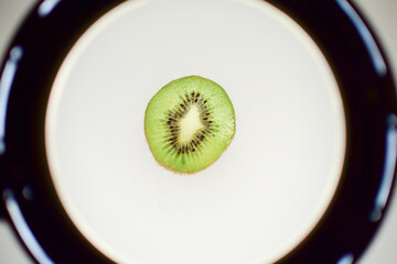 Half-cut kiwi fruit on a white plate against a black background