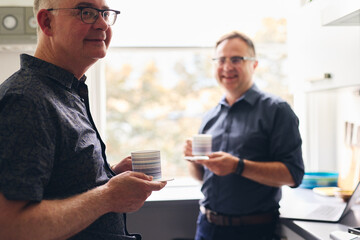 Smiling same sex couple drinking coffee in apartment kitchen