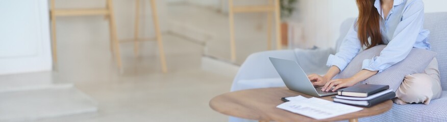 Business at home concept, Businesswoman sitting on couch to typing marketing plan report on laptop