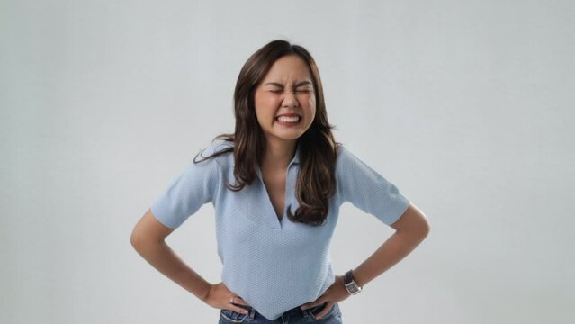 A woman from Asia wearing a light blue shirt, looking like she has a stomach ache and needs to use the restroom. Isolated on a white background.