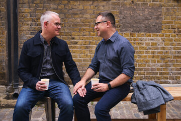 Same sex couple drinking coffee and chatting outside coffee shop