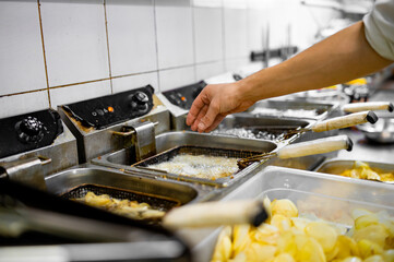 Chef cooking delicious potato chips in hot oil on kitchen