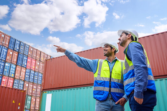 Two Engineers or foreman container cargo wearing white hardhat and safety vests checking stock into container for loading from Cargo freight ship for import export. industry worker of logistic concept