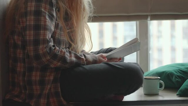 Teen girl sits on the windowsill and reads a book