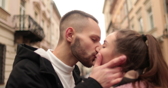 Close-up of the faces of a young couple in love kissing and hugging on the street on a gloomy autumn day.