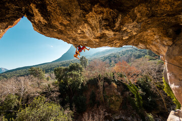 A young rock climber on an overhanging cliff. The climber climbs the rock. The girl is engaged in...