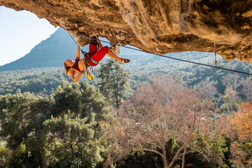 Obraz premium A young rock climber on an overhanging cliff. The climber climbs the rock. The girl is engaged in sports climbing.