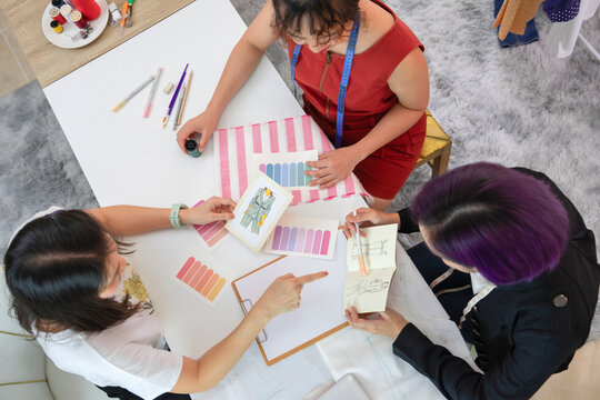 top view young female fashion designer and tailor discussing clothing design to woman customer with fashion sketch and color sample (selective focus), concept of business,industry,design,tailoring
